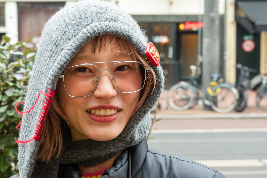 Street portrait of a woman wearing glasses, a gray hood, and a scarf in Amsterdam