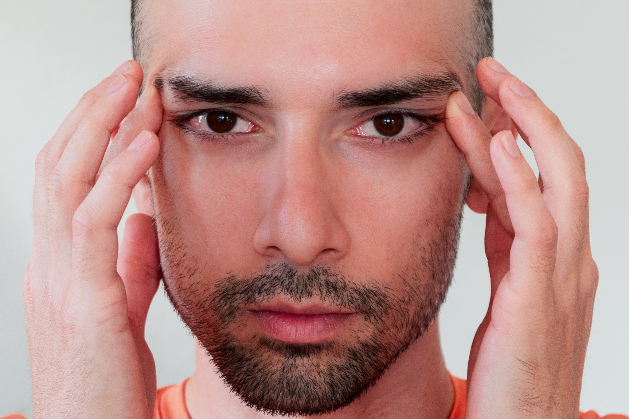 Close-up portrait of a man touching his temples against a light background