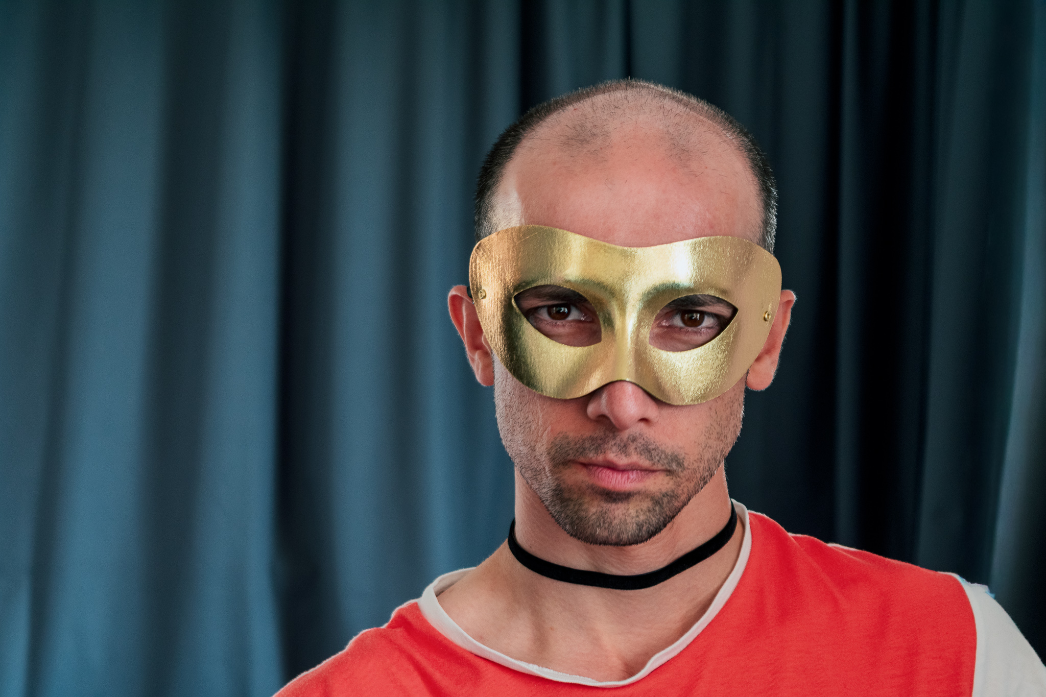 Portrait of a man wearing a gold mask against dark curtains