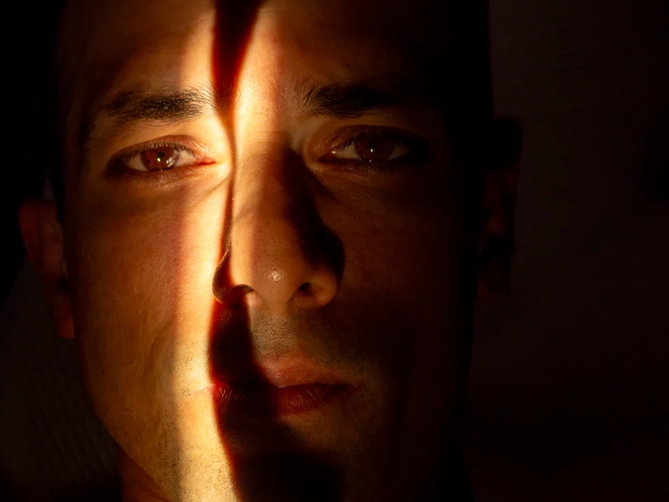 Close-up portrait of a man with a narrow band of warm light across his face and deep shadows